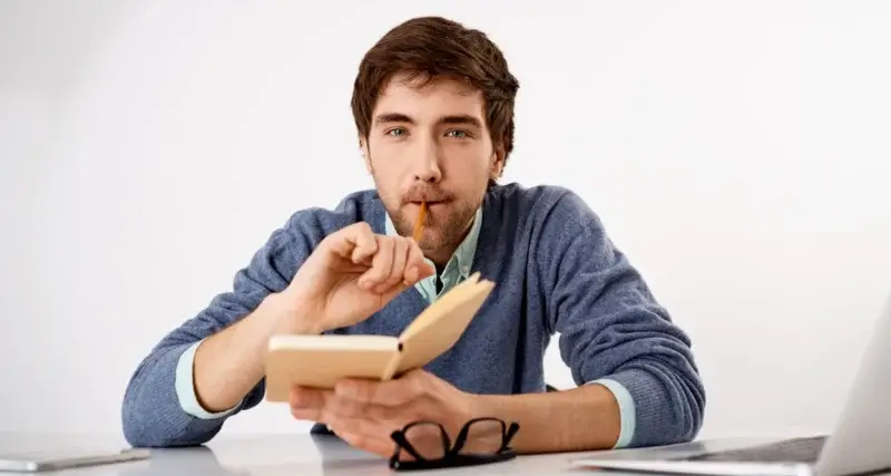 Homem pensando com um livro e uma caneta na mão